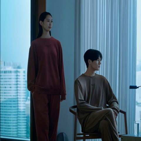 BAKUNEを着て窓辺に立つ女性と椅子に座る男性