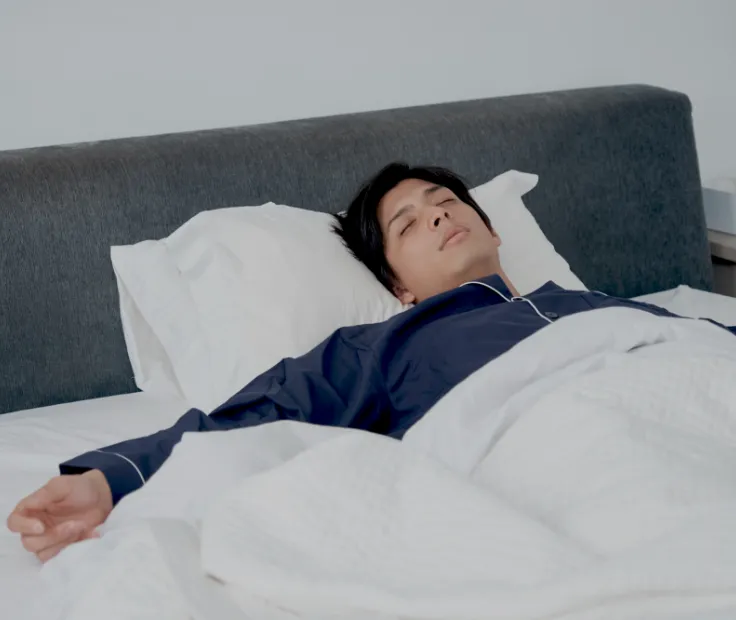 掛け布団をずらして眠る男性のイメージ写真